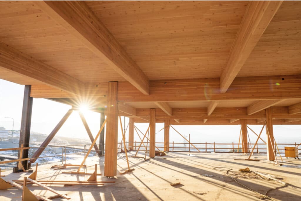 Upper floor of building in the middle of being constructed, wood beams, ceiling and floor. Sun shining through the open areas of the construction site