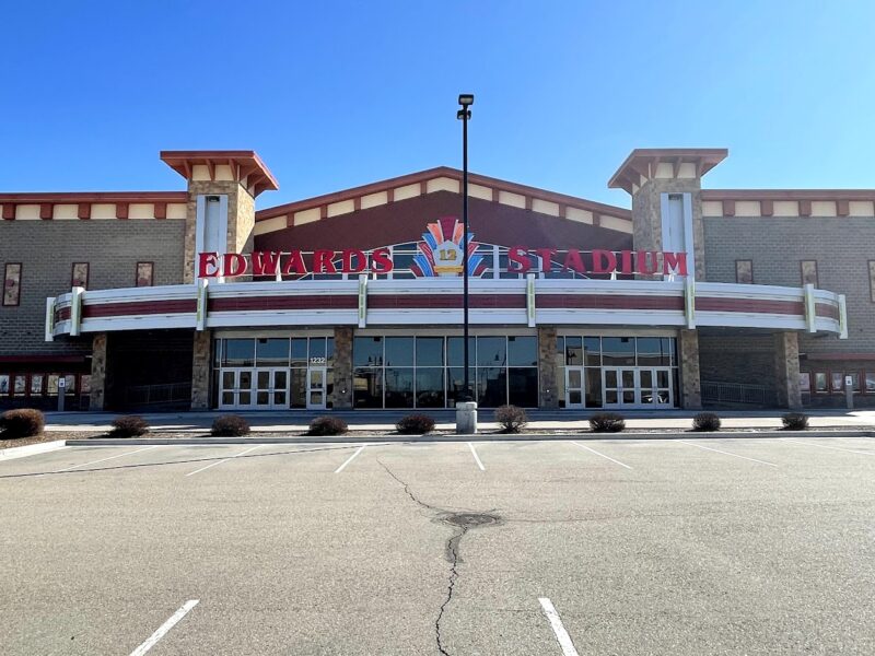 Front view of the Edwards 12 Stadium movie theater with a large, retro-style marquee and an empty parking lot under a clear blue sky.